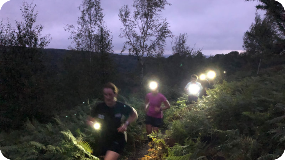 Group of trail runners running in the Surrey Hills at night with head torches.